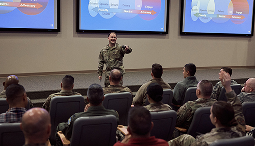 Military personnel are seated in a large classroom as the teacher points to a student.