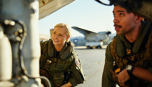 Two military personnel looking at the undercarriage of an aircraft.